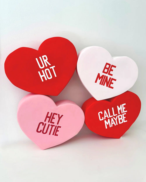 Four heart-shaped candy sculptures with Valentine's Day text on a white background