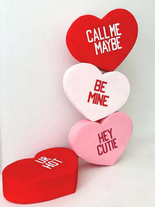 Four heart-shaped sculptures with romantic phrases on a white background
