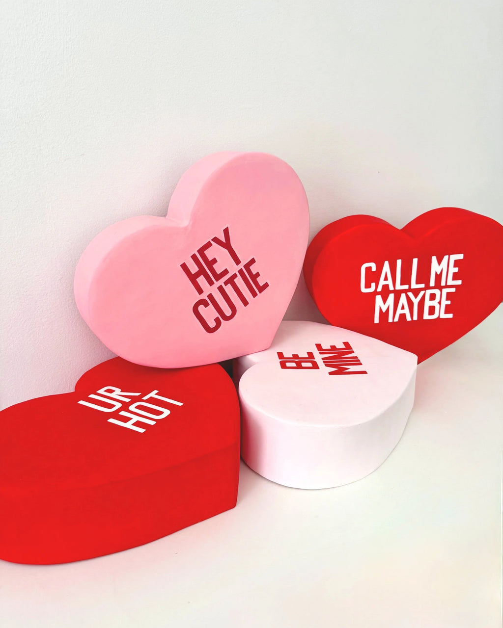 Four heart-shaped sculptures with Valentine's Day phrases on a white background
