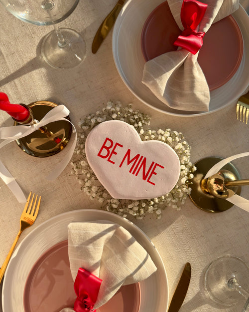 Valentine's Day table setting with white heart-shaped 'BE MINE' scultpure, red napkins, and gold cutlery.