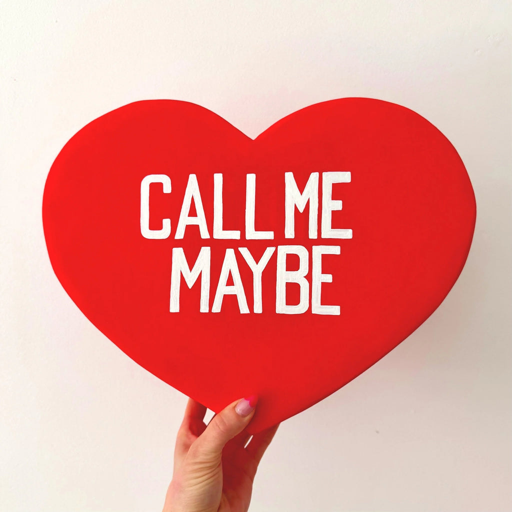 Red heart-shaped sculpture with 'Call Me Maybe' text held by a hand on a white background