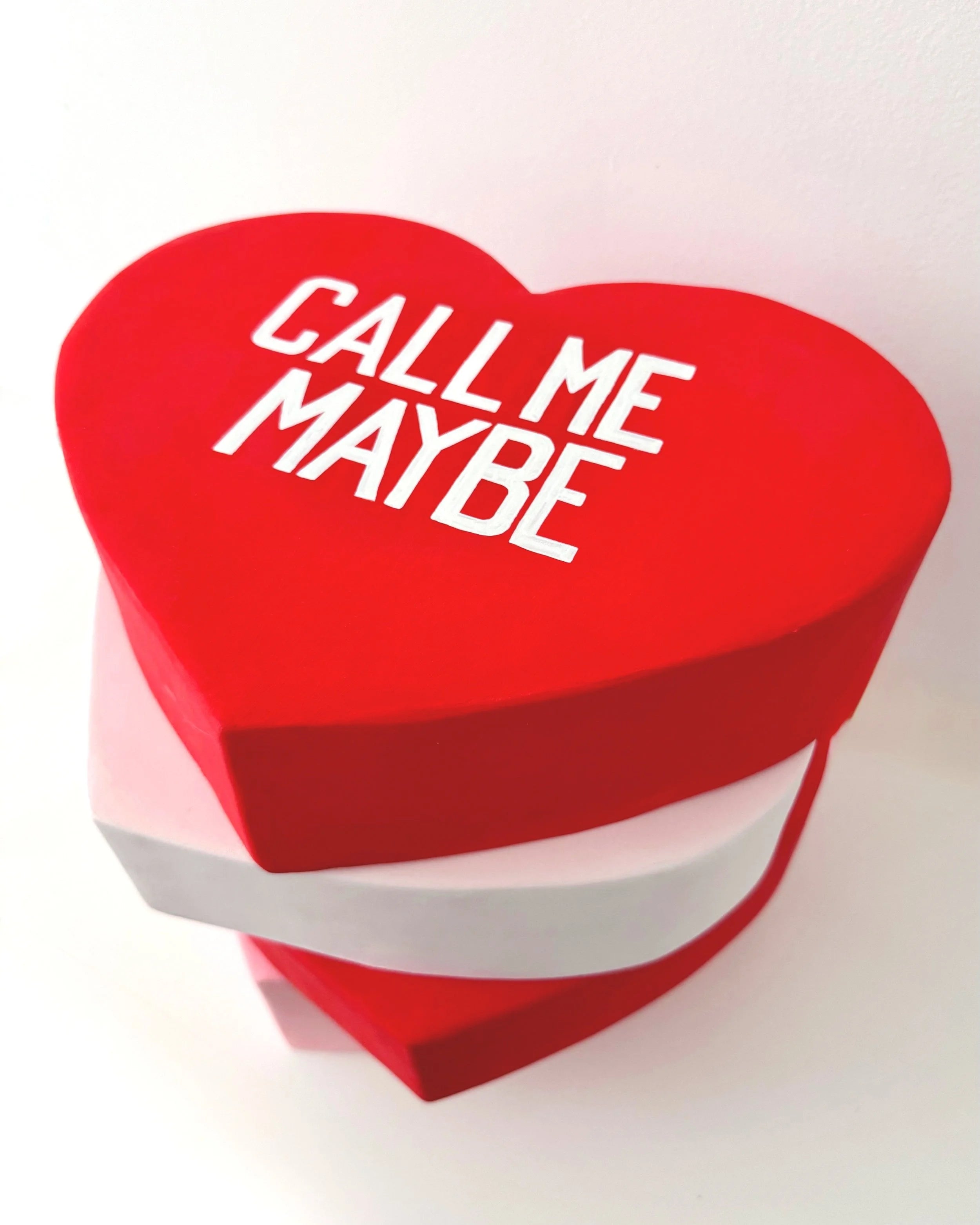 Red heart-shaped sculpture with 'Call Me Maybe' text on a white background