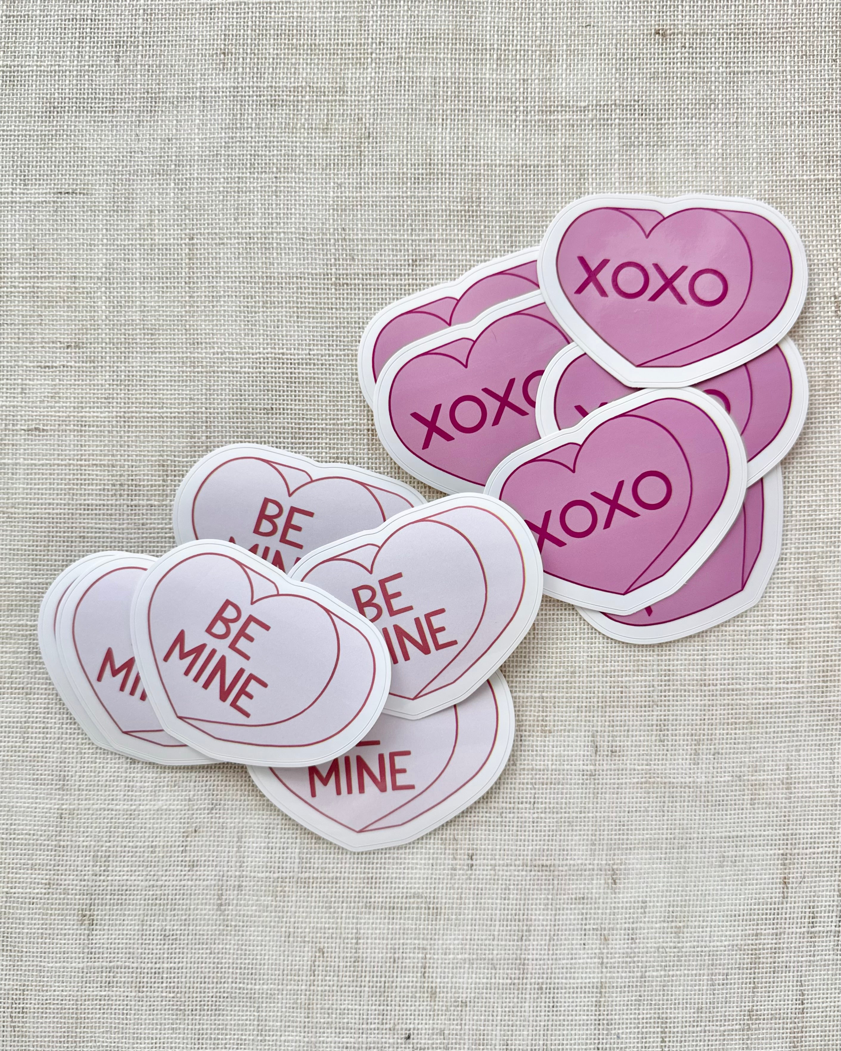 Heart-shaped stickers with 'XOXO' and 'Be Mine' text on a textured fabric background