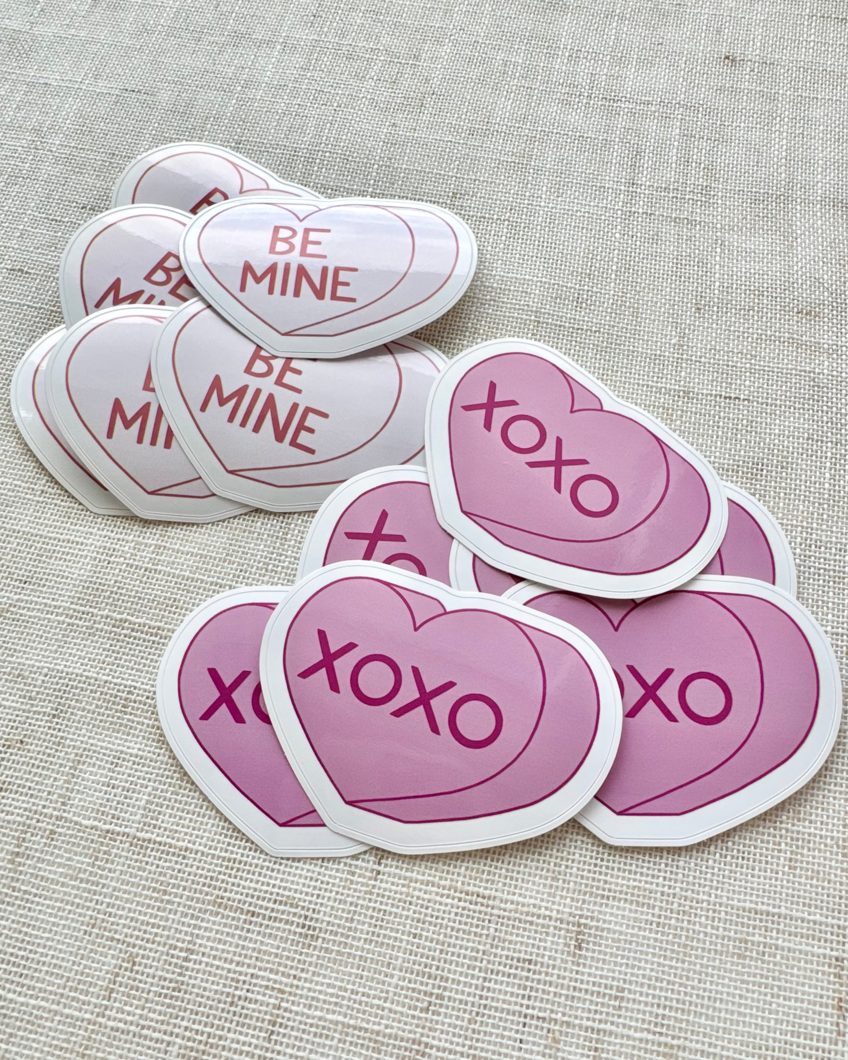 Heart-shaped stickers with 'BE MINE' and 'XOXO' text on a textured surface