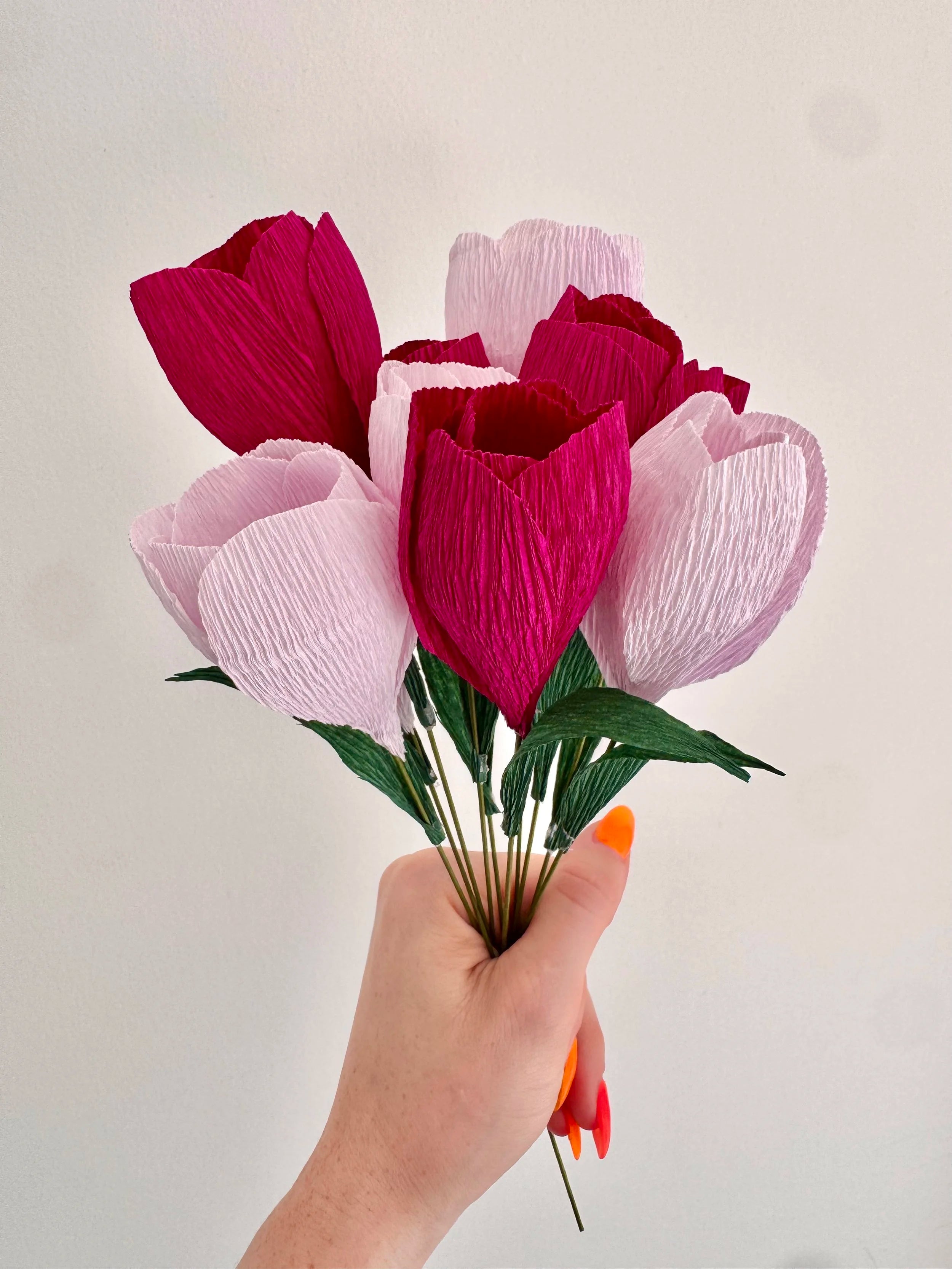 Hand holding a bouquet of light and dark purple crocuses against a light background
