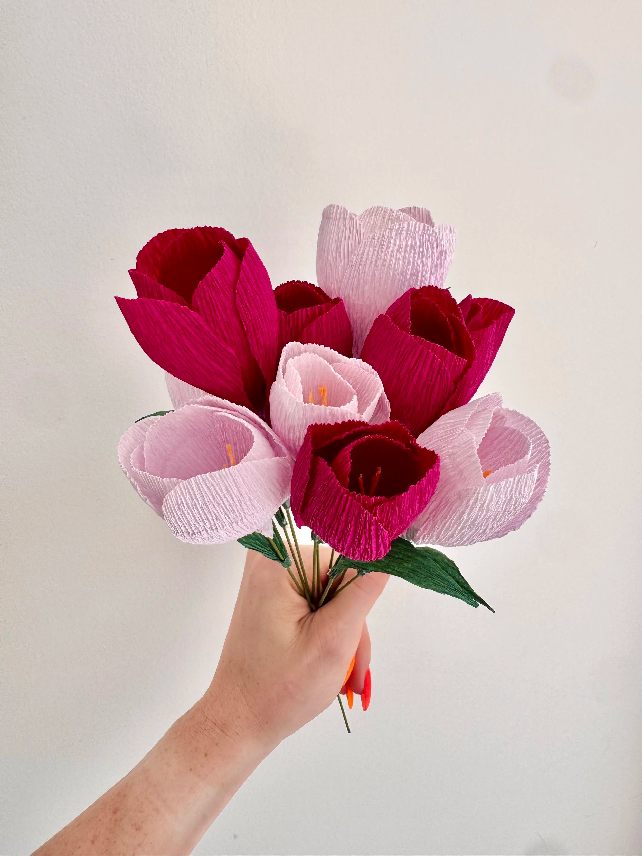 Hand holding a bouquet of light and dark purple crocuses against a light background