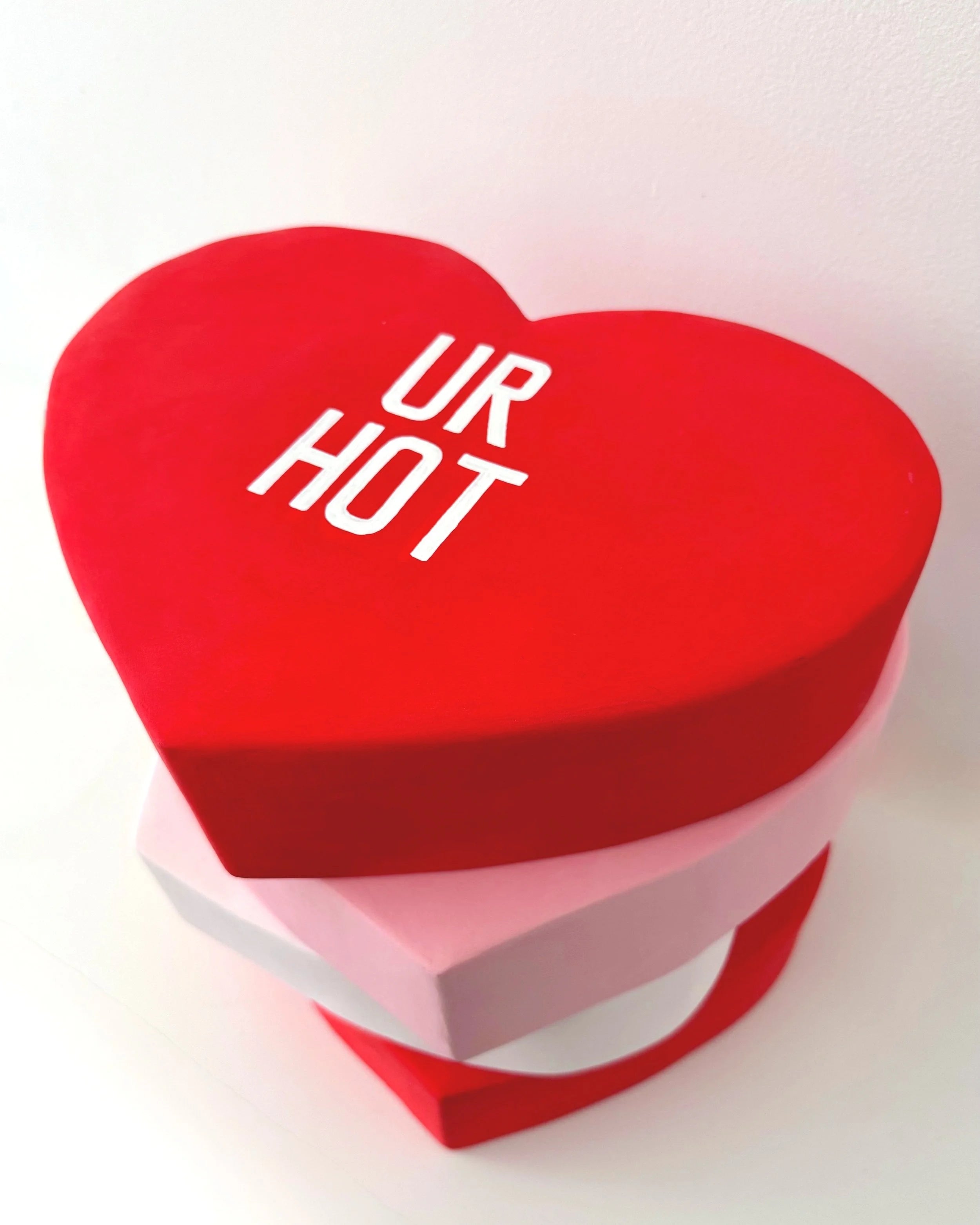 Heart-shaped red sculpture with 'UR HOT' text on a white background