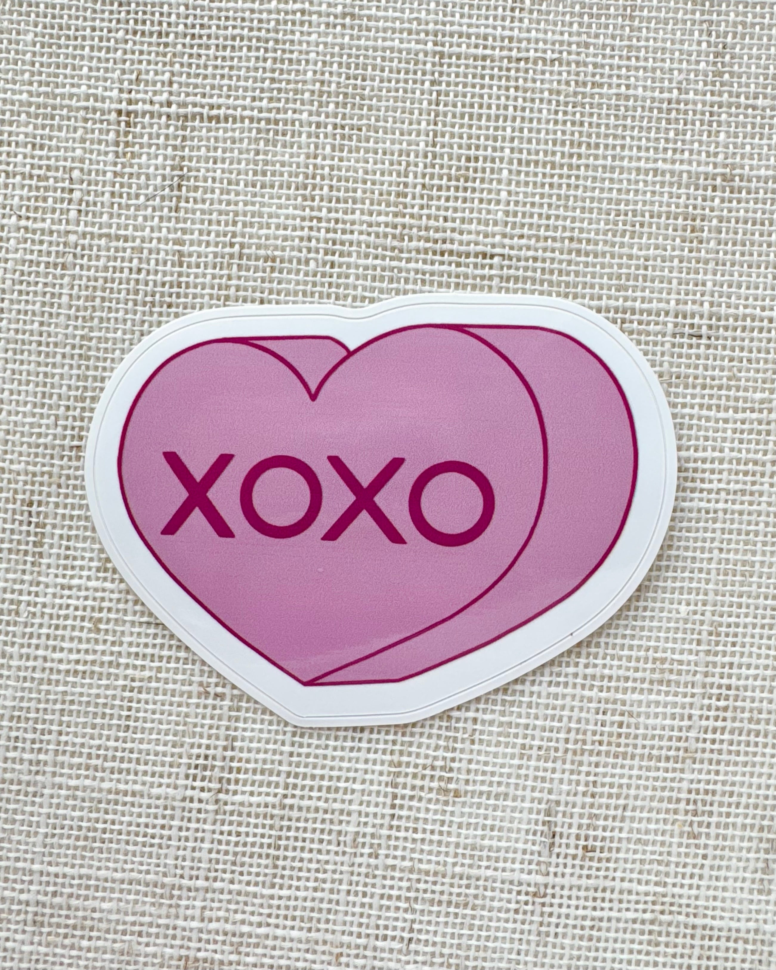 Heart-shaped sticker with 'XOXO' text on a textured beige background