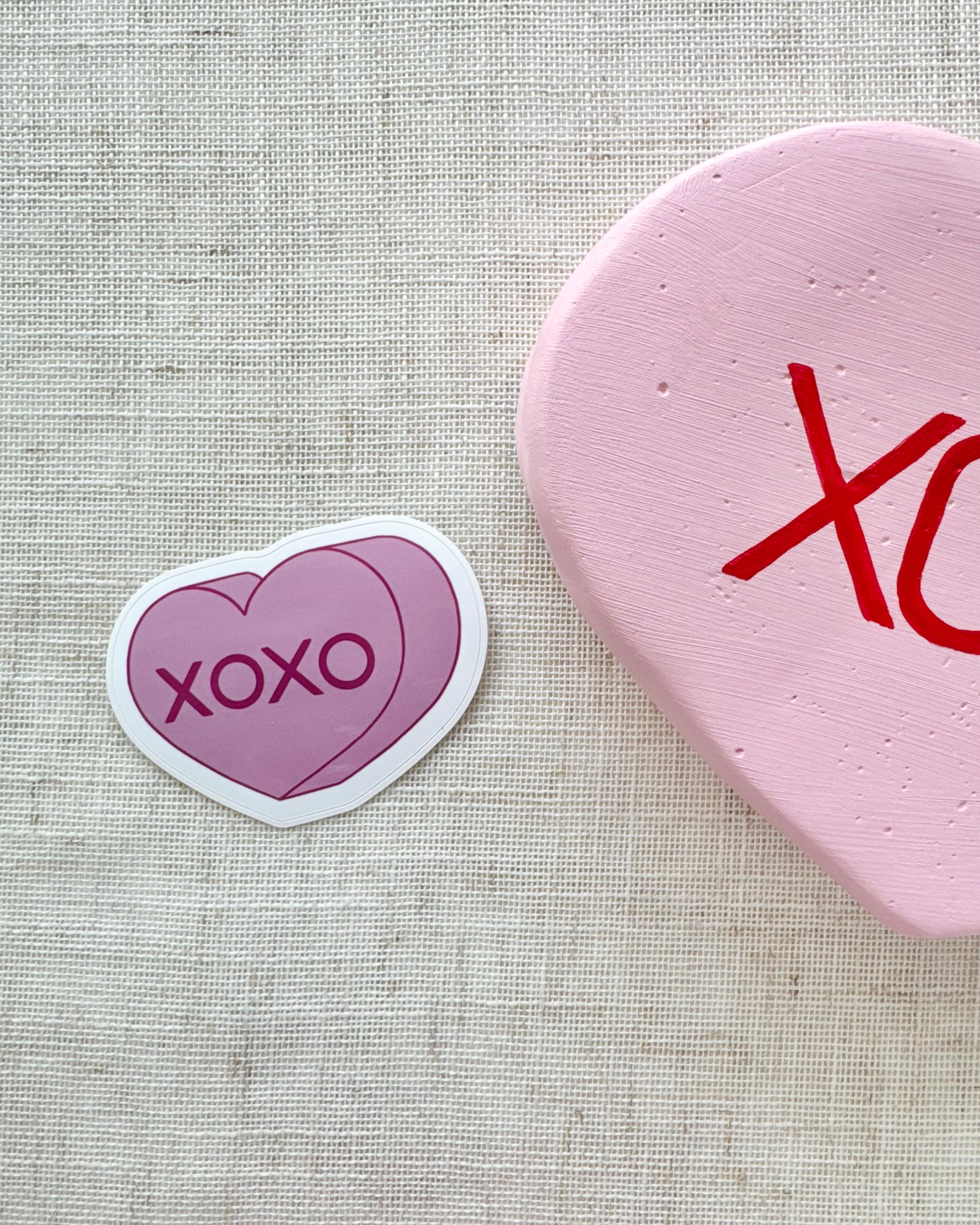 Two heart-shaped stickers with 'XOXO' on a textured fabric background