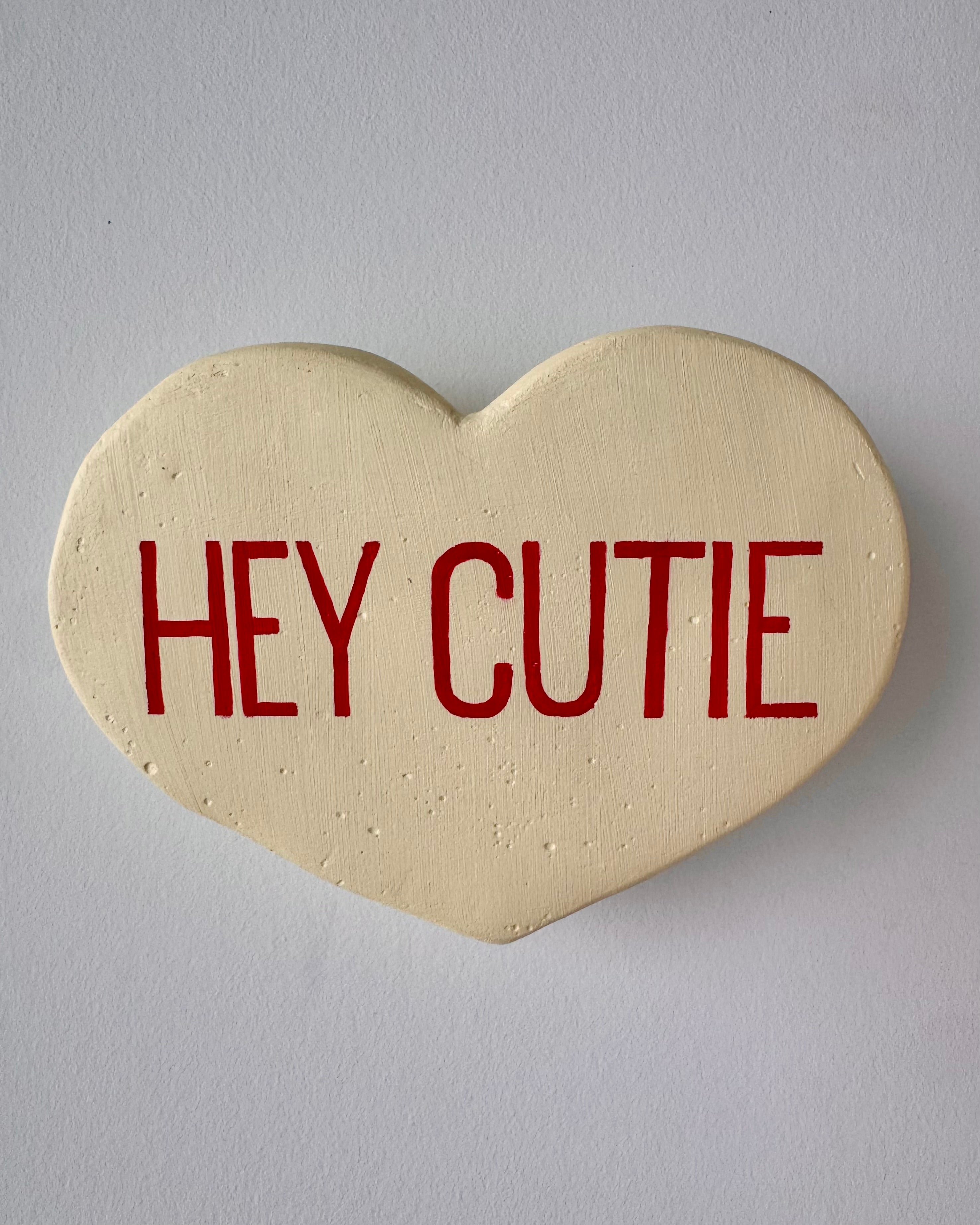 Yellow heart-shaped sculpture with 'HEY CUTIE' text on a plain background