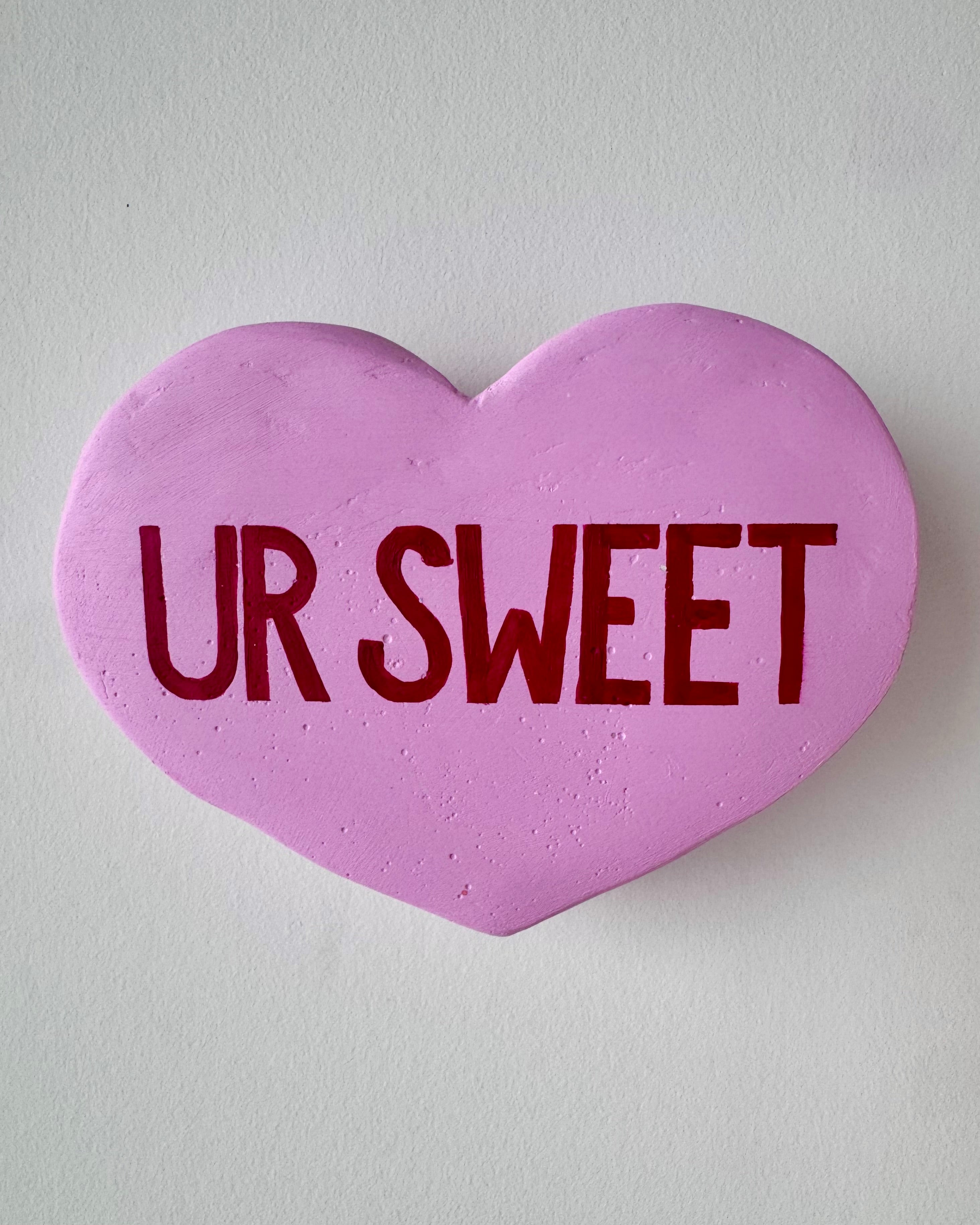 Light purple heart-shaped sculpture with 'UR SWEET' text on a light gray background