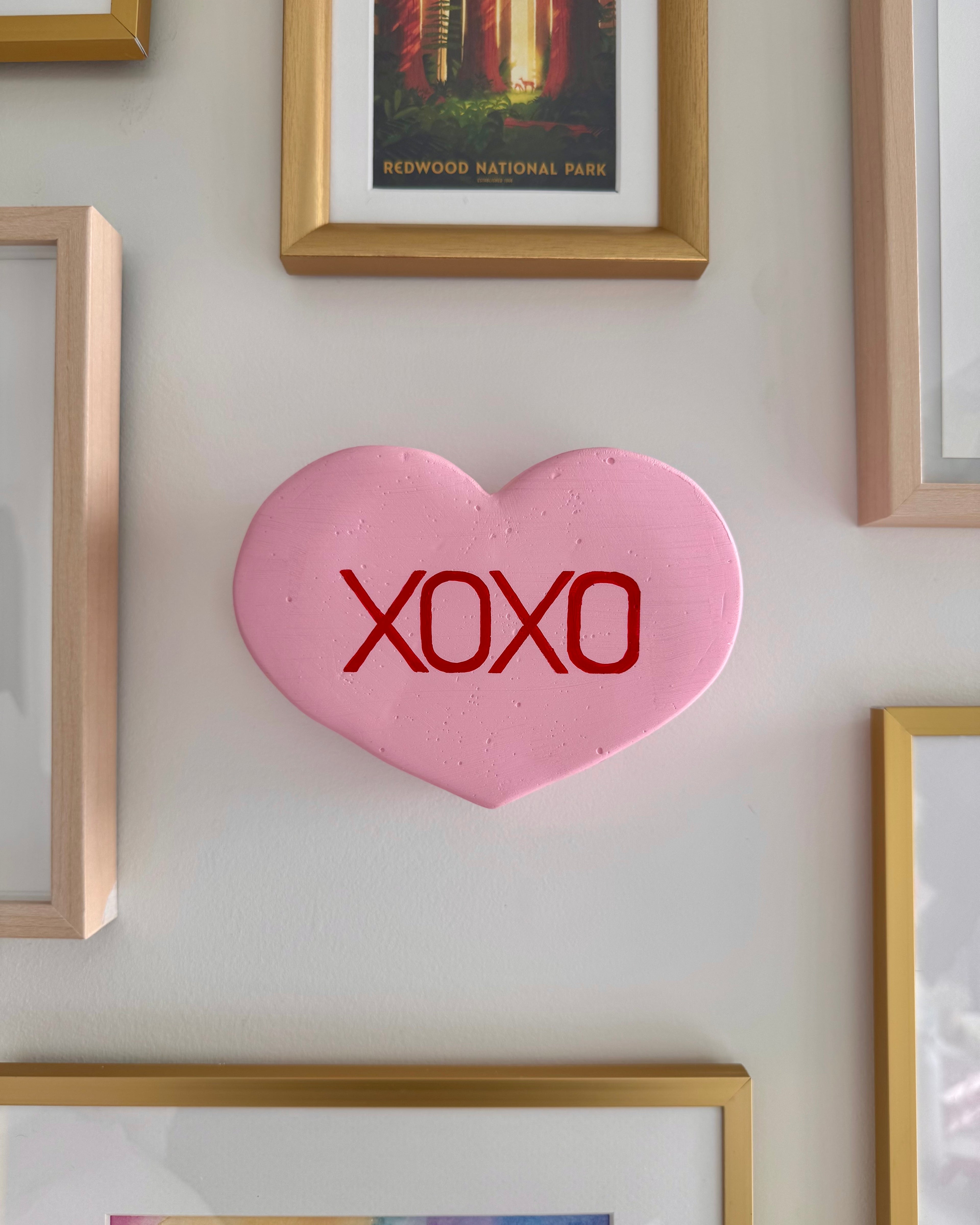 Pink heart-shaped sculpture with 'XOXO' on a wall with framed pictures