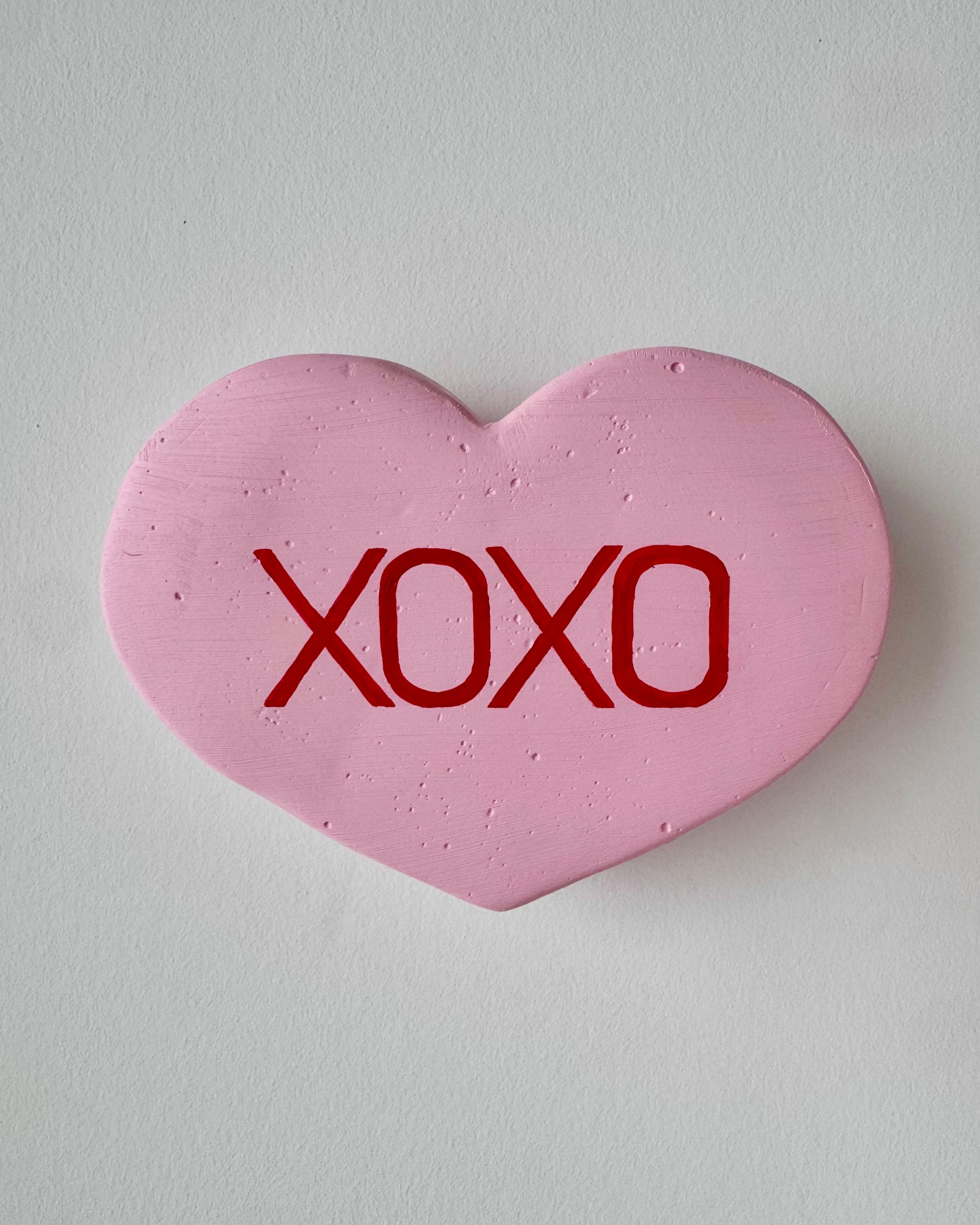 Pink heart-shaped sculpture with 'XOXO' text on a light gray background